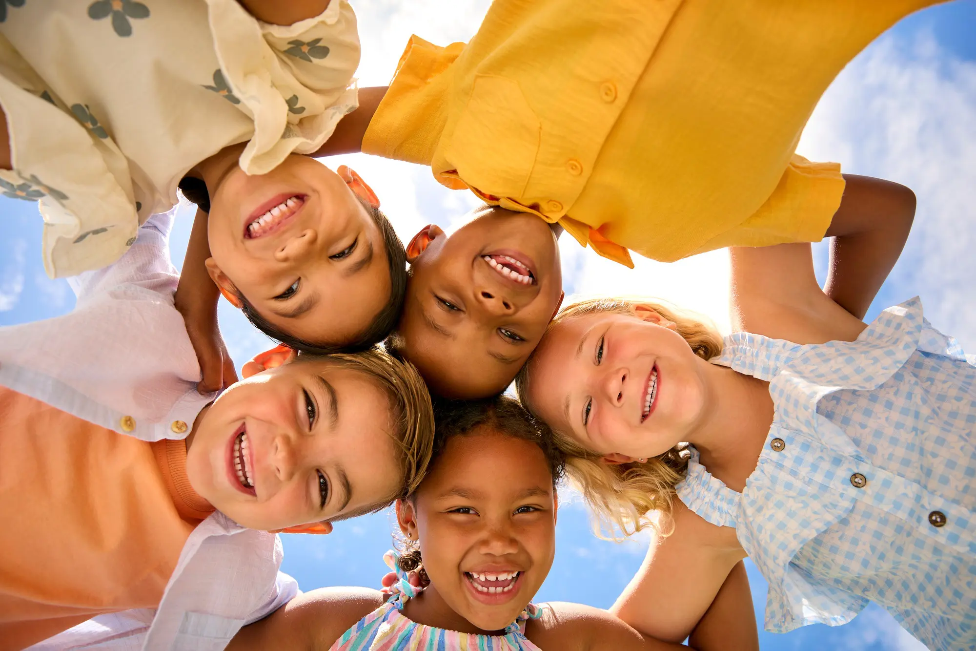 Group Of Multi-Cultural Children Friends Linking Arms Looking Down Into Camera